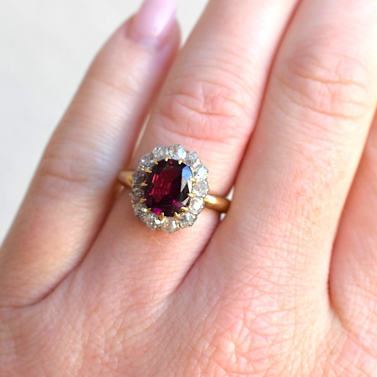 Antique Belle Epoque 18k gold ring with 2.5ct rubellite garnet and old cut diamond halo worn on a feminine hand