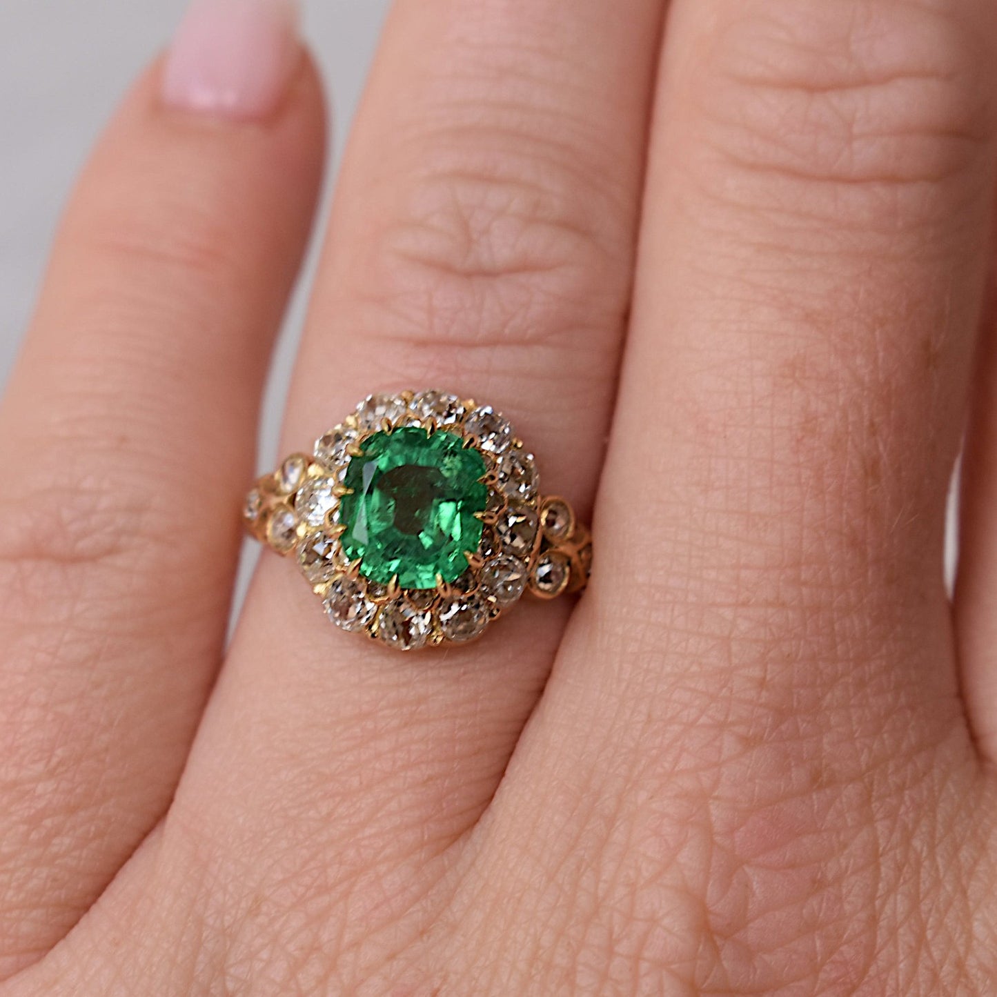 Close-up shot of the hand wearing the 13x12.5mm Bellerophon-certified emerald cocktail ring, highlighting the ring's scale and brilliant sparkle against the skin.