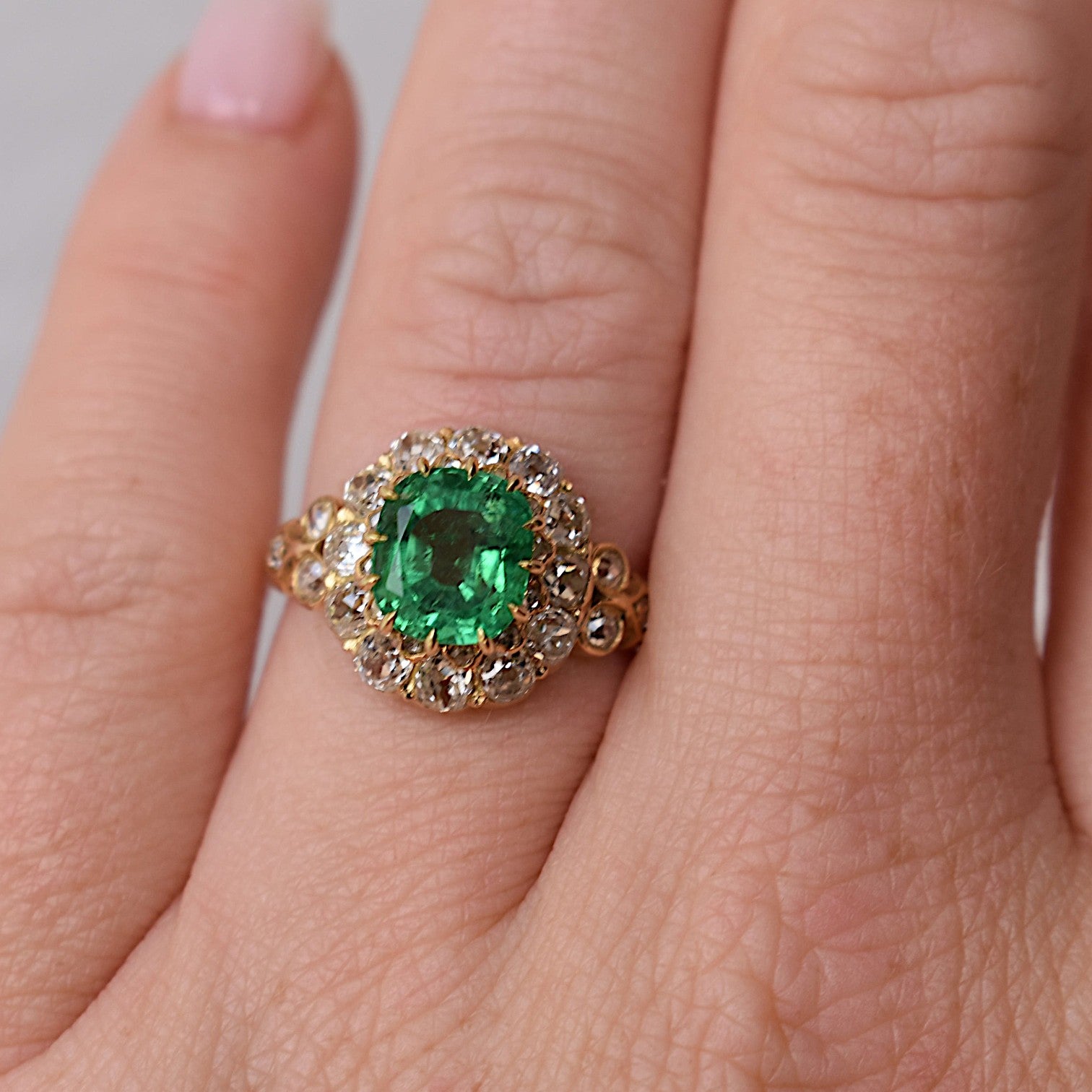Close-up shot of the hand wearing the 13x12.5mm Bellerophon-certified emerald cocktail ring, highlighting the ring's scale and brilliant sparkle against the skin.