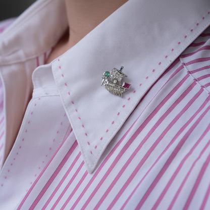 Extreme close-up shot of the multi-gemstone Viking ship pin styled on a tie, highlighting its historic scale, color contrast, and sparkle against dark fabric.