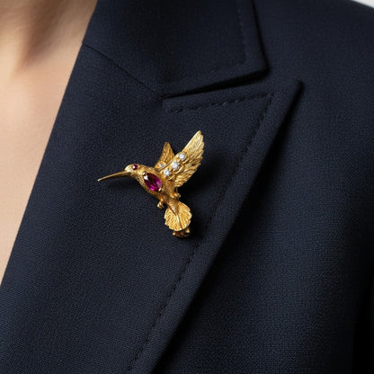 Signed British luxury hummingbird pin styled elegantly on a cashmere scarf, highlighting its delicate scale and vivid rubies.