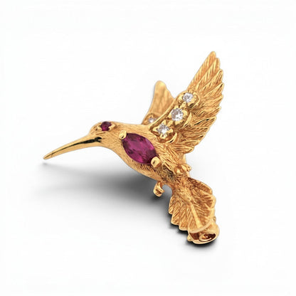 Detailed macro shot of the 18k gold hummingbird's head showcasing the natural ruby eye and sparkling diamond accents.