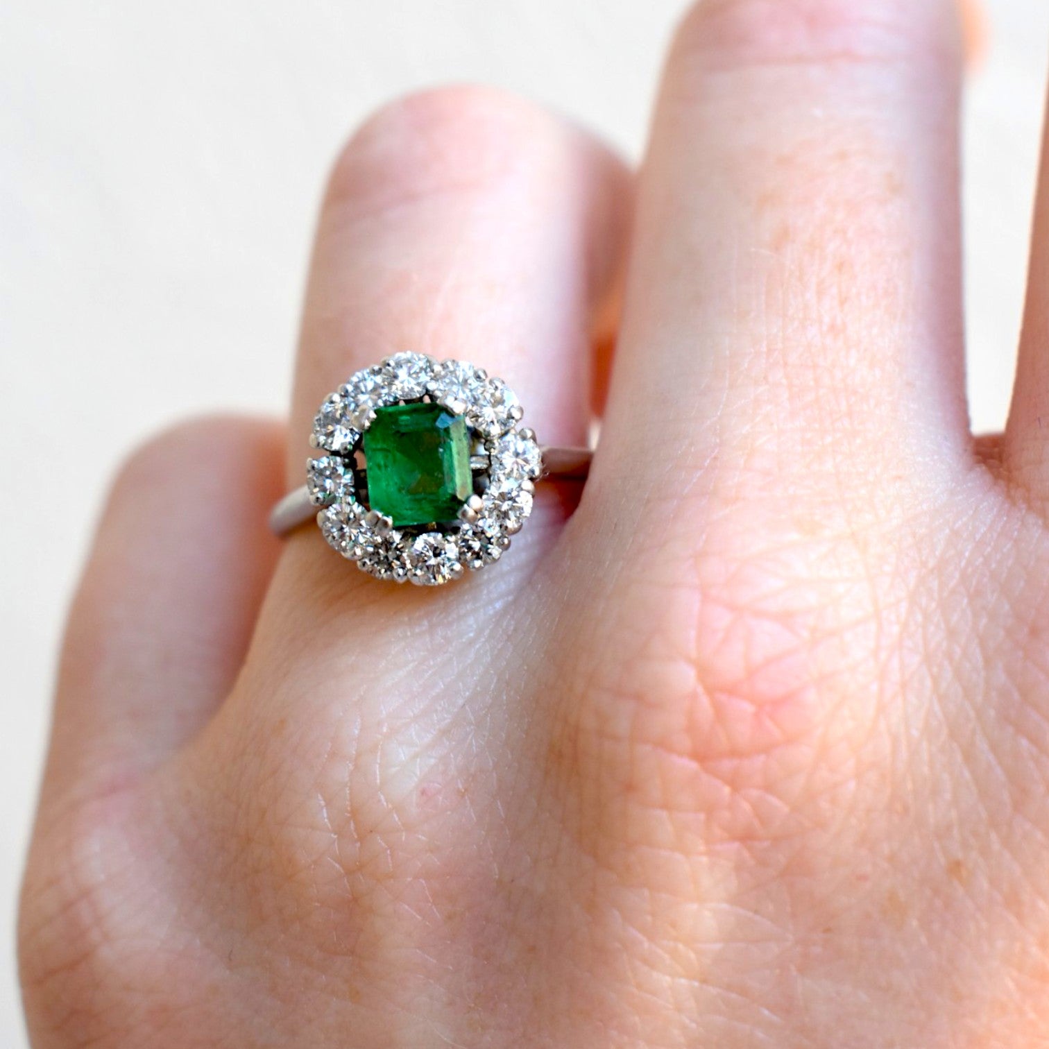 Close-up of vintage emerald ring surrounded by 12 brilliant cut diamonds worn at natural light