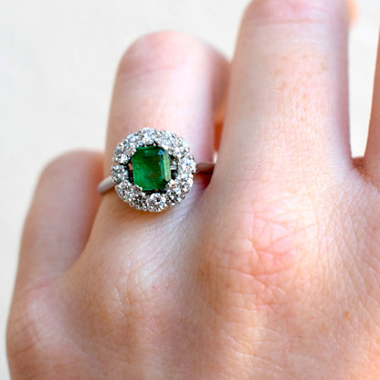 Close-up of vintage emerald ring surrounded by 12 brilliant cut diamonds worn at natural light