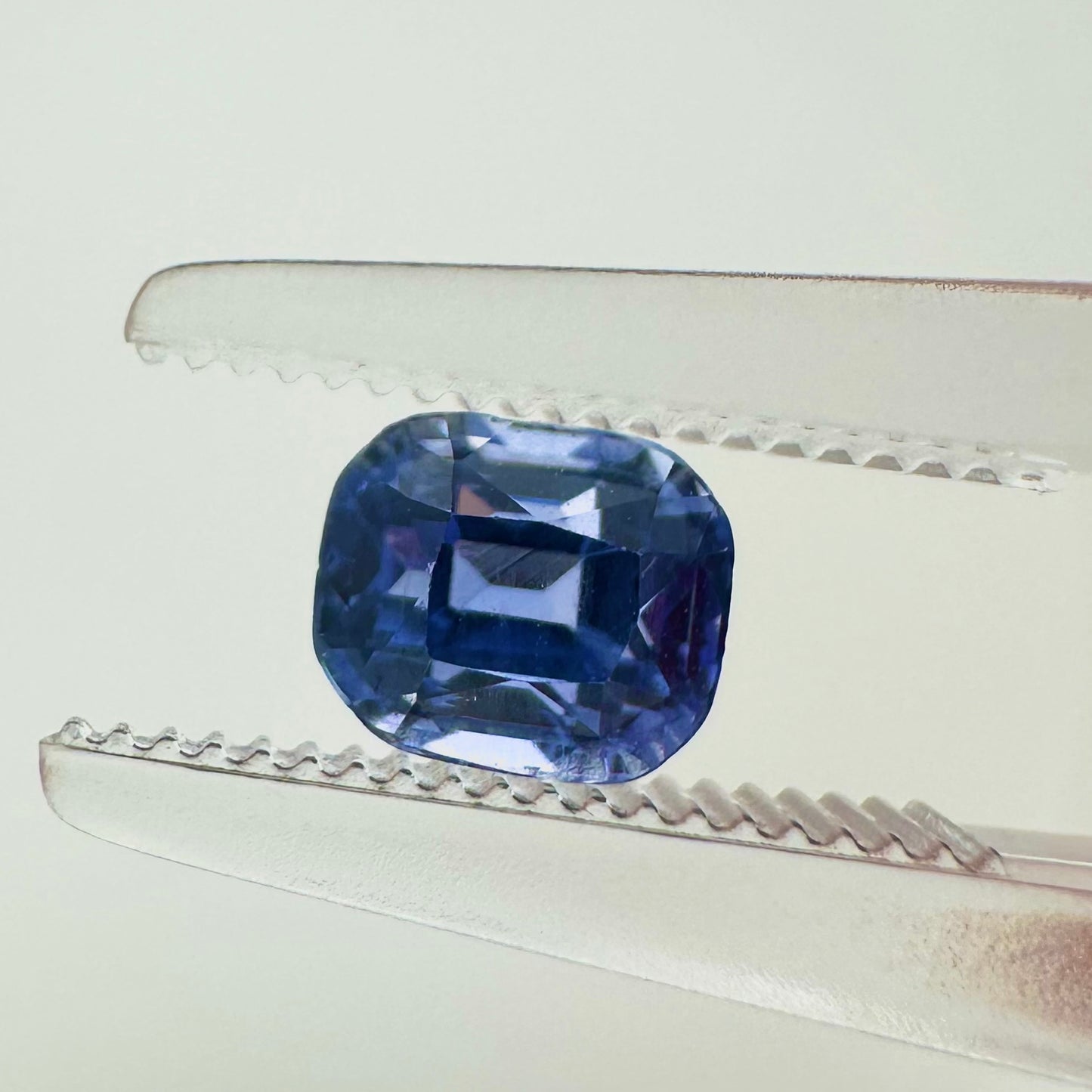 Extreme macro face shot of the 0.89ct natural blue Ceylon sapphire showcasing its elegant step-cut emerald shape and clean geometric facets.