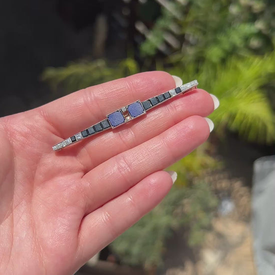 High-definition video capturing the intense blue of the lapis lazuli, the sleek black luster of the onyx, and the ultra-bright, fiery brilliance of the D-color diamonds on the geometric 1920 Art Deco platinum bar brooch in motion.