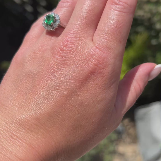 High-definition video capturing the vivid green glow of the 1-carat natural emerald, the fiery brilliance of the surrounding diamond daisy halo, and the authentic Mellerio signature and serial number engraved on the polished platinum band in motion.