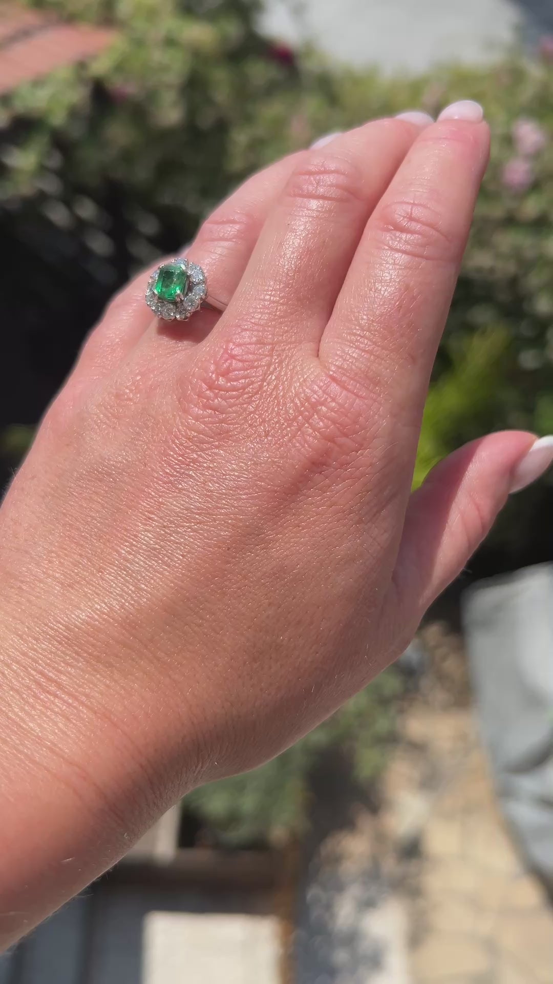 High-definition video capturing the vivid green glow of the 1-carat natural emerald, the fiery brilliance of the surrounding diamond daisy halo, and the authentic Mellerio signature and serial number engraved on the polished platinum band in motion.