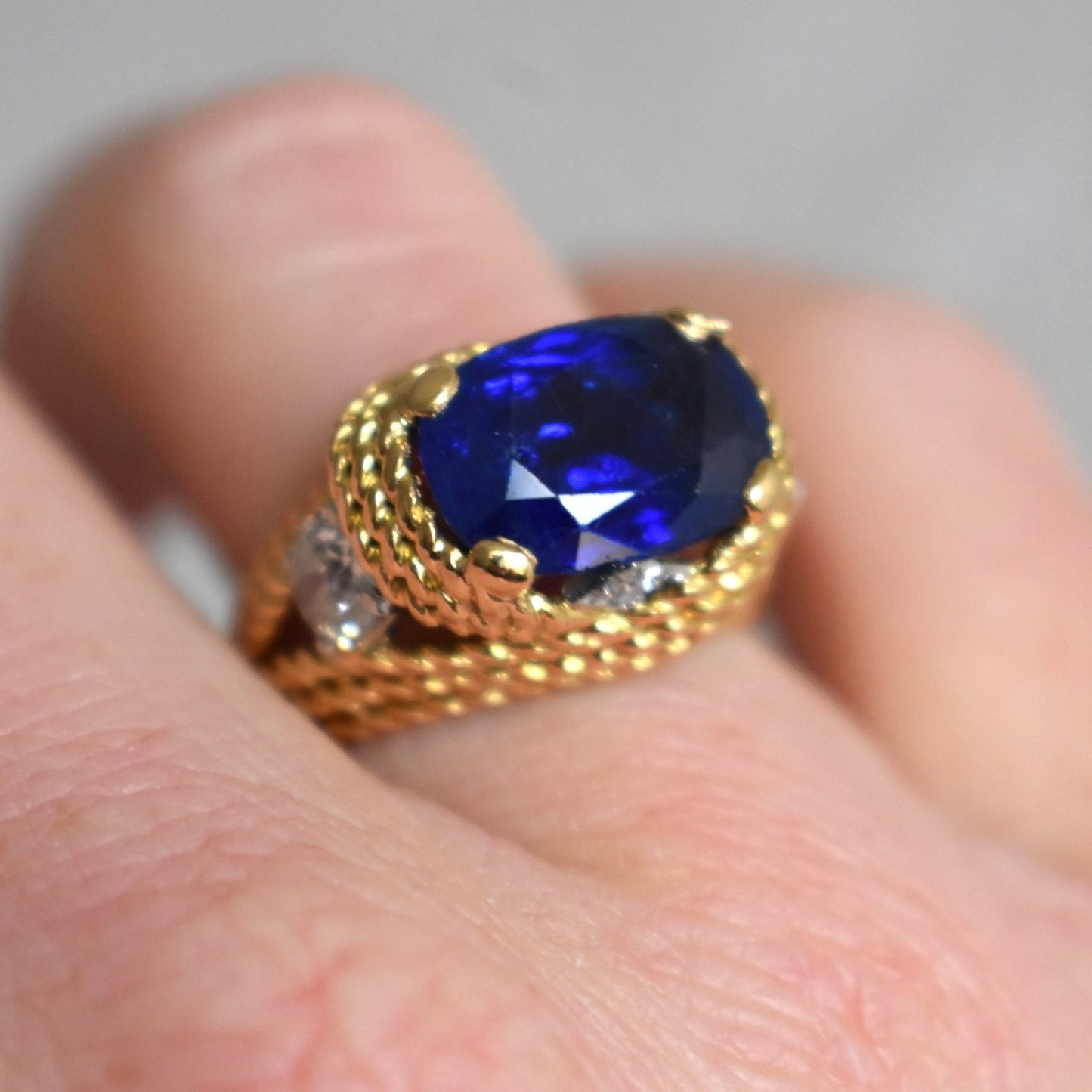Extreme close-up shot of the 13mm wide unheated sapphire ring on hand, highlighting its luxurious scale and fire under natural light.